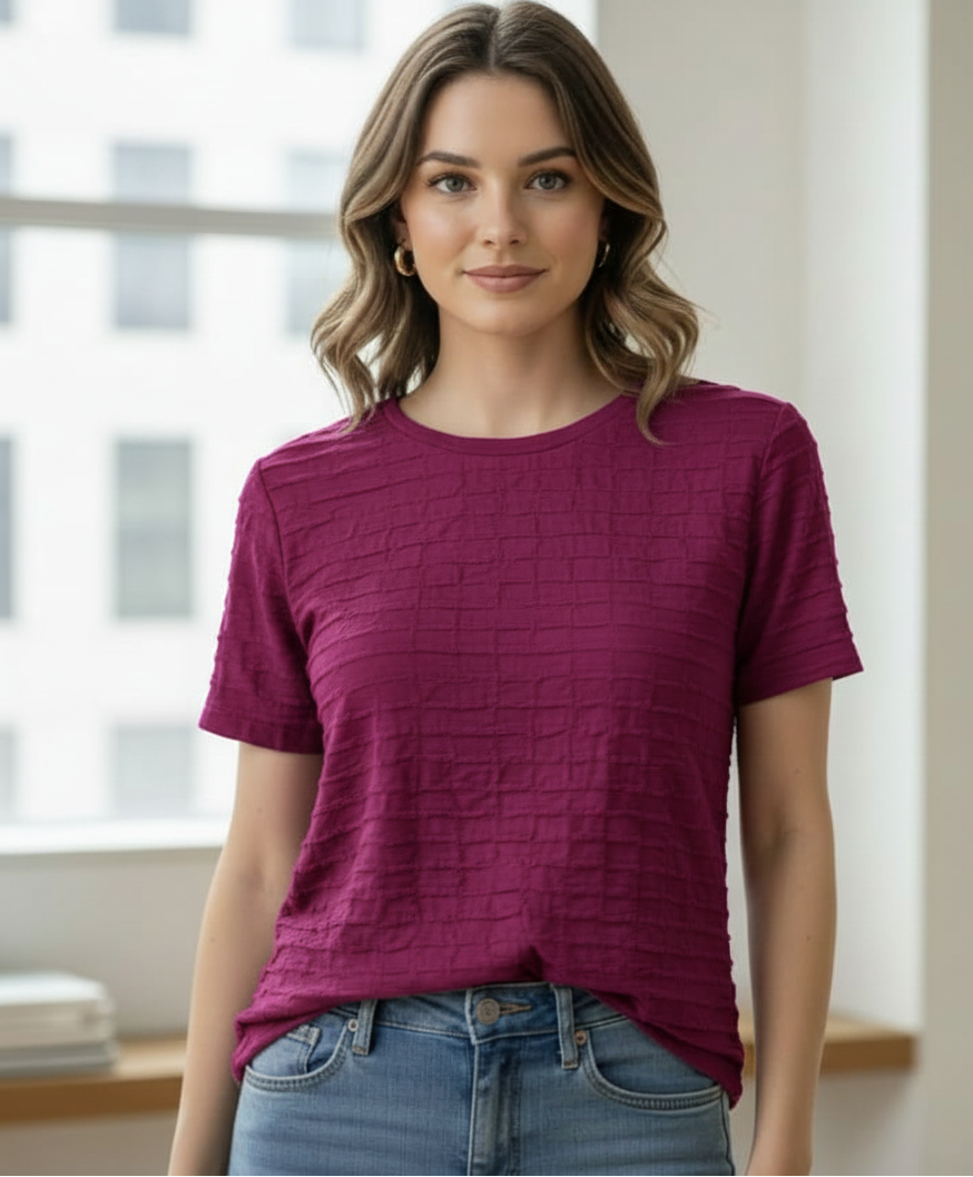 Woman wearing a textured purple t-shirt and blue jeans indoors.